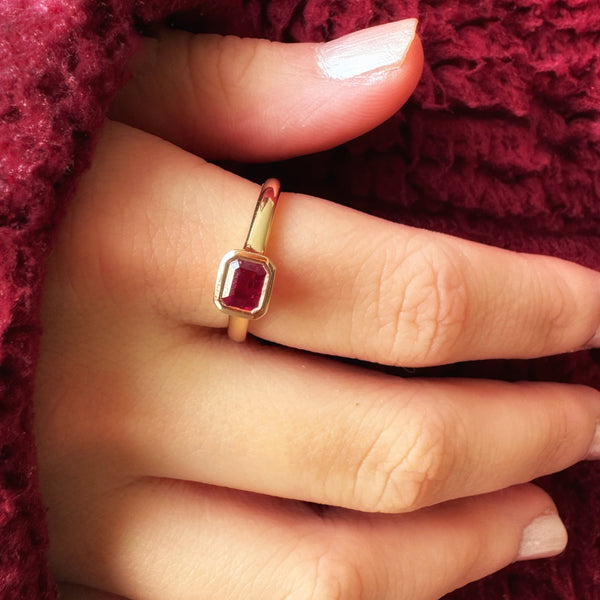 Gold ring with a red ruby on a hand against a red textured background